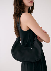 Black hobo bag worn on shoulder by woman in matching dress against white background