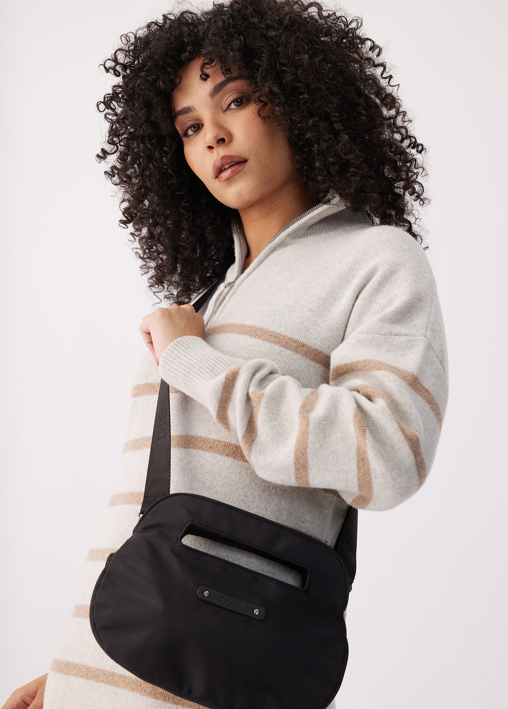 Black crossbody bag with top handle and adjustable strap, worn over shoulder on model