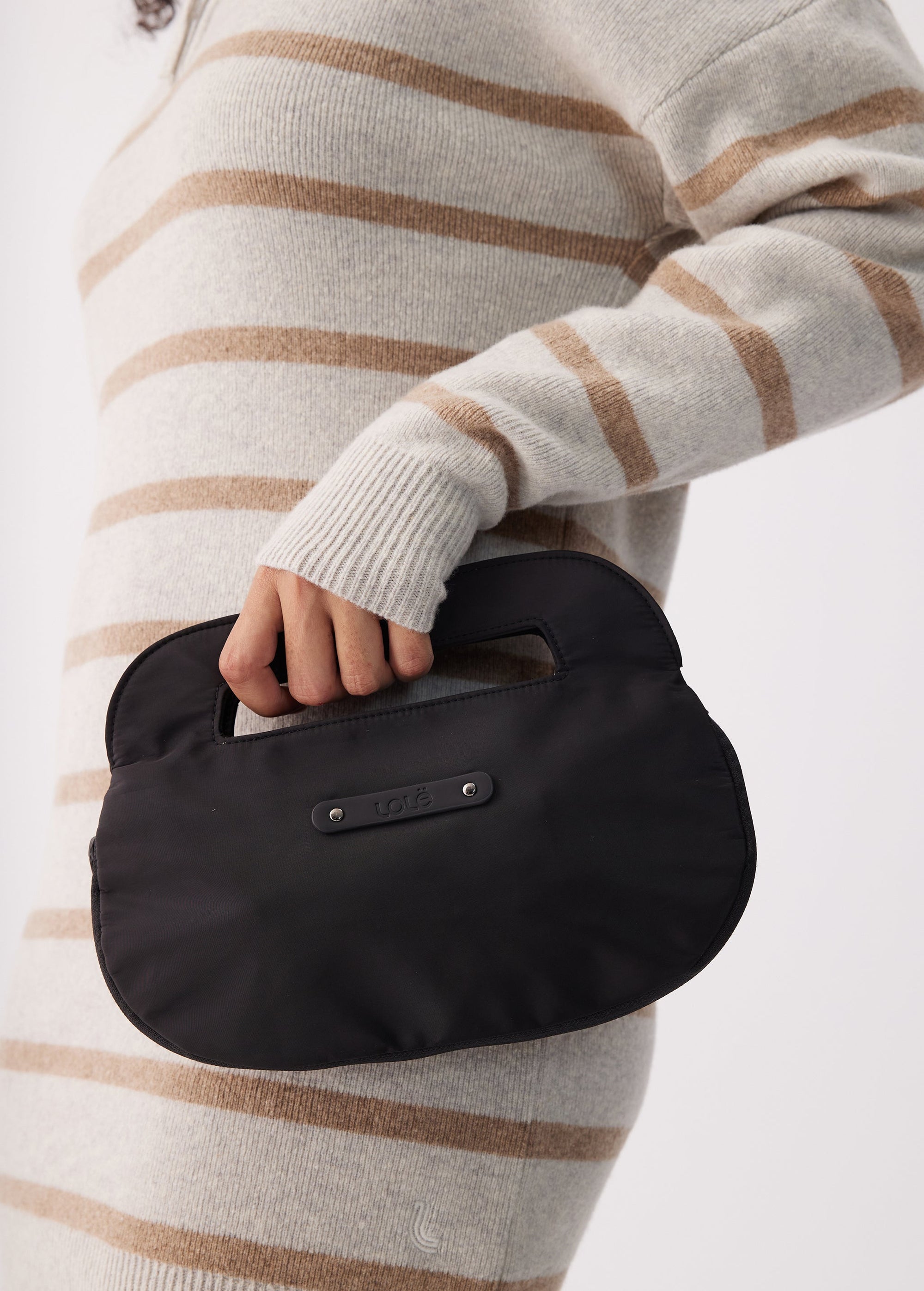 Small black rounded handbag with top handle, held by model in striped sweater