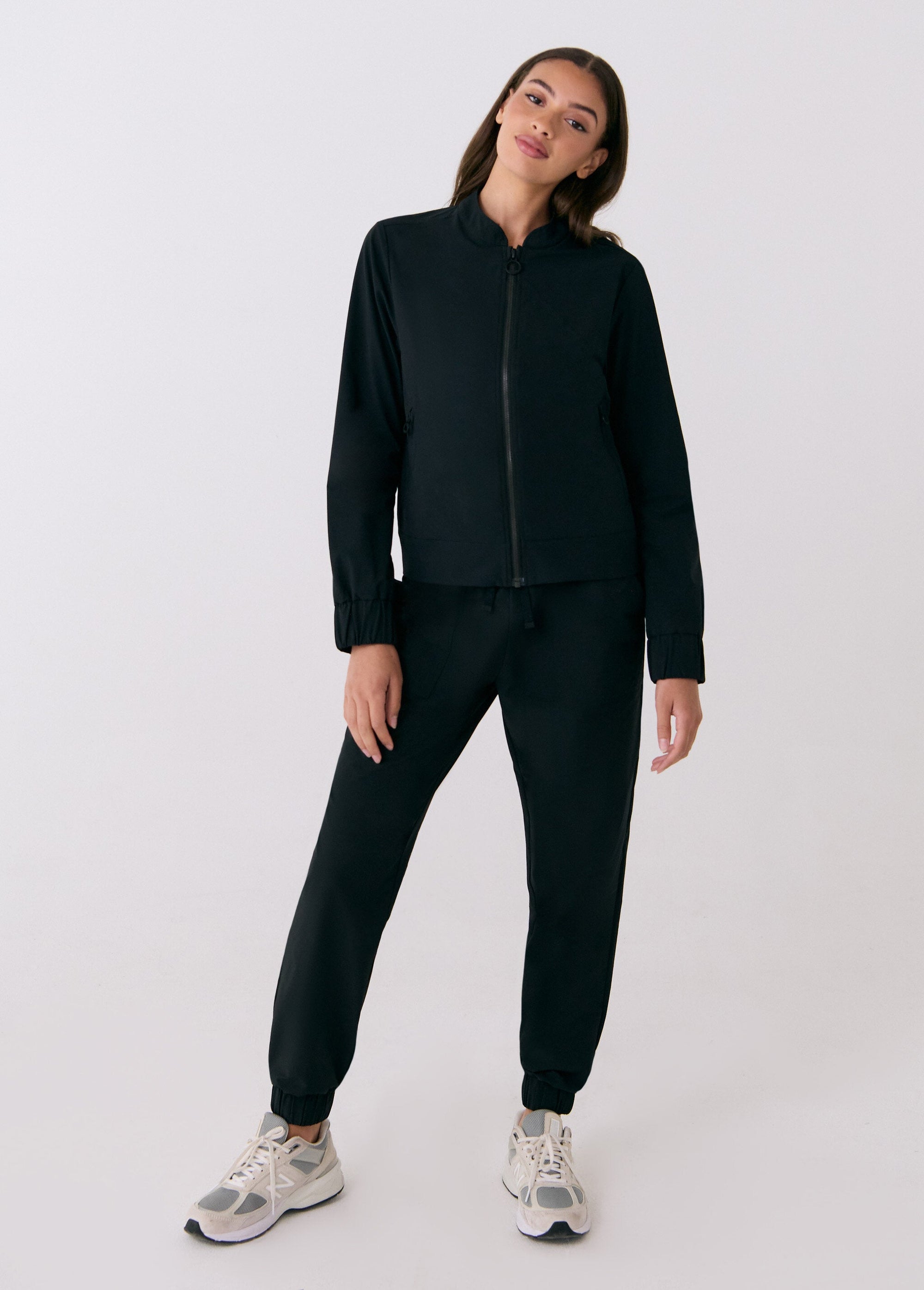 Black zip-up travel jacket with stand collar, worn with matching jogger pants, front view