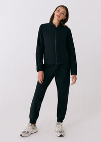 Black zip-up travel jacket with stand collar, worn with matching jogger pants, front view