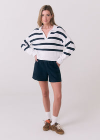 White and navy striped polo sweater with V-neck and ribbed hem, styled with dark shorts