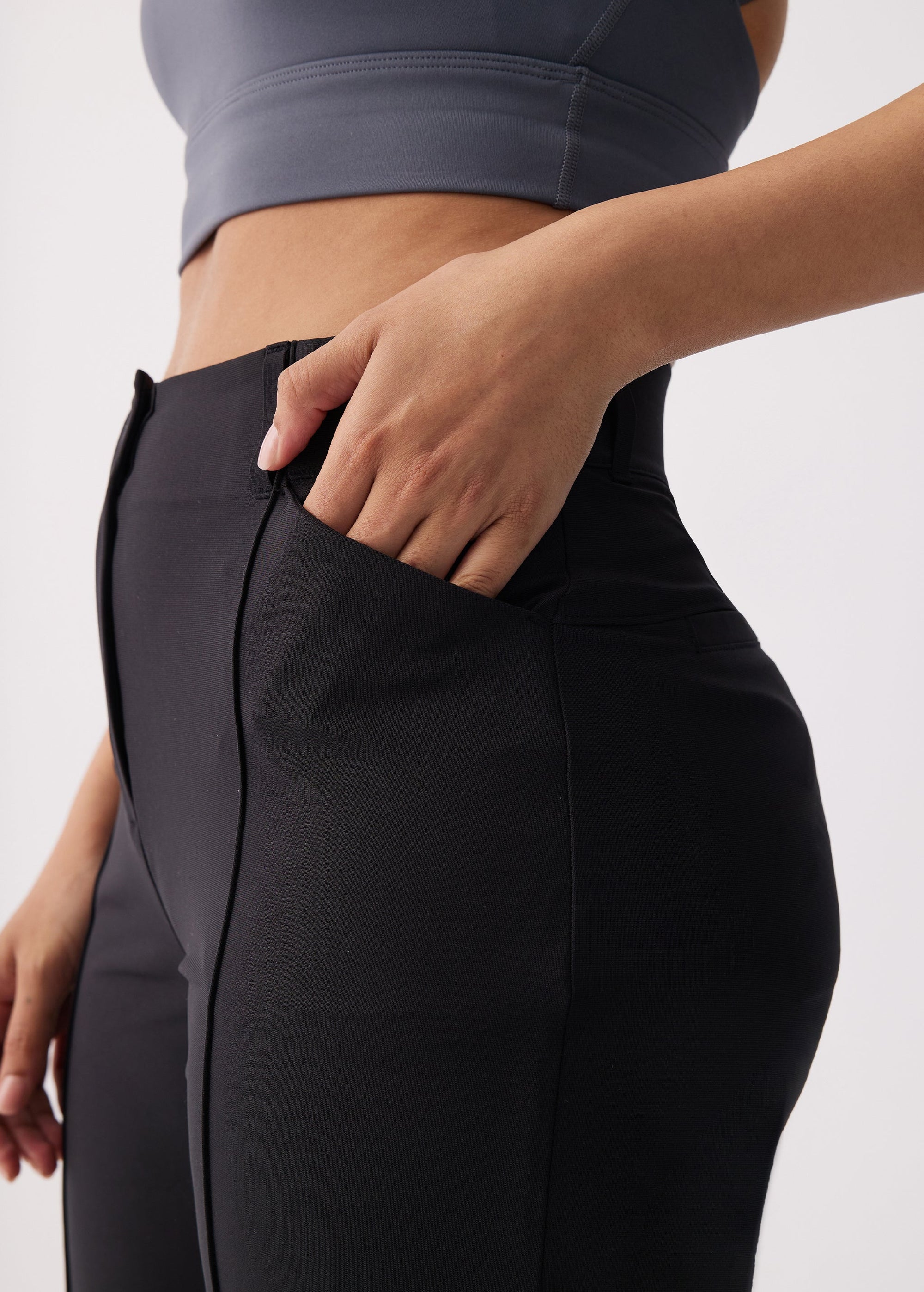 Close-up detail of black travel trousers showing zippered side pocket with hand inserted