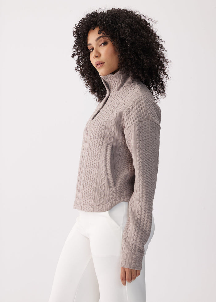 Women's cable-knit mock neck long sleeve top in taupe, side view on model with white pants