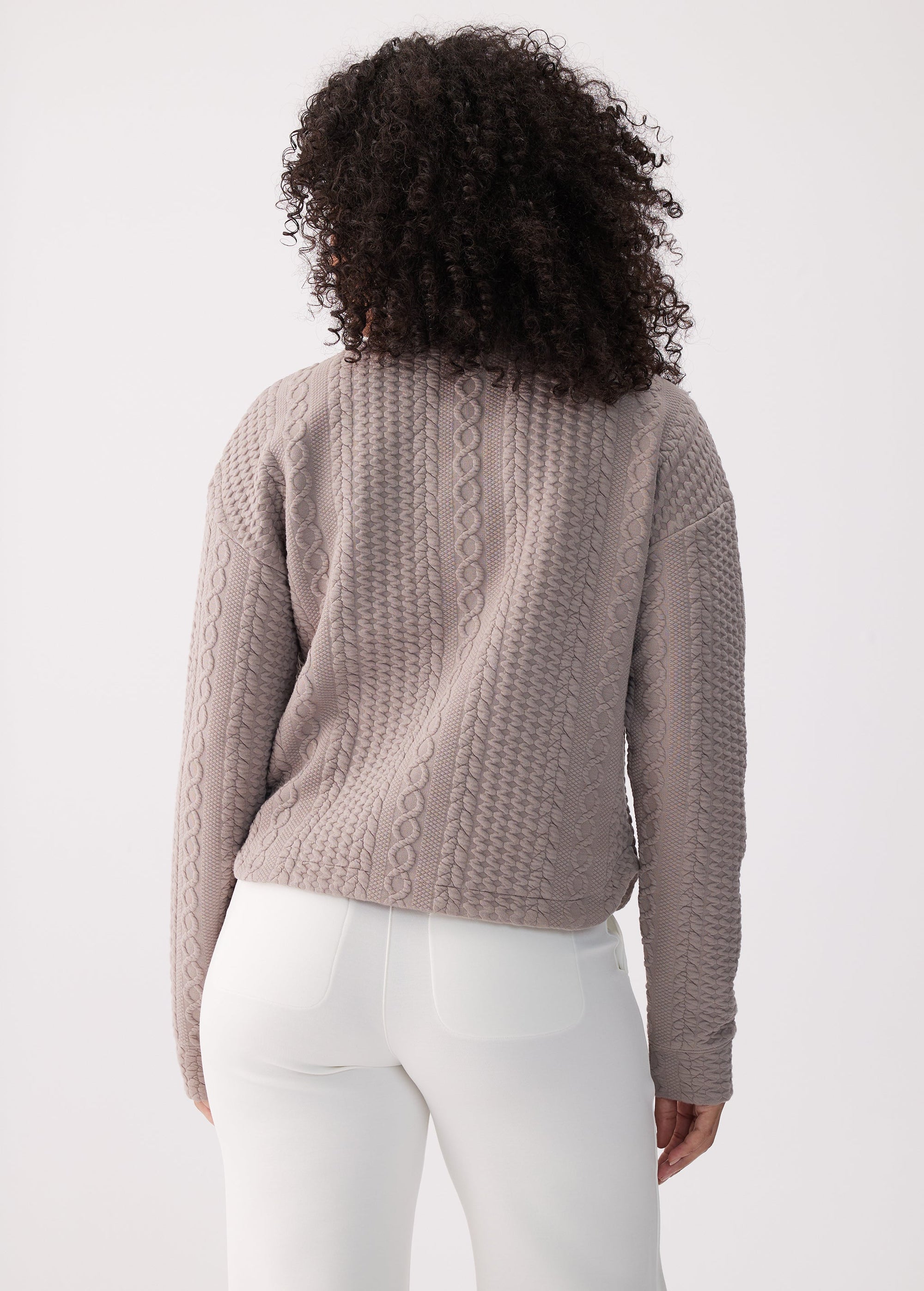 Cable-knit long sleeve pullover top in taupe, back view on model with white pants