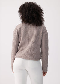 Cable-knit long sleeve pullover top in taupe, back view on model with white pants