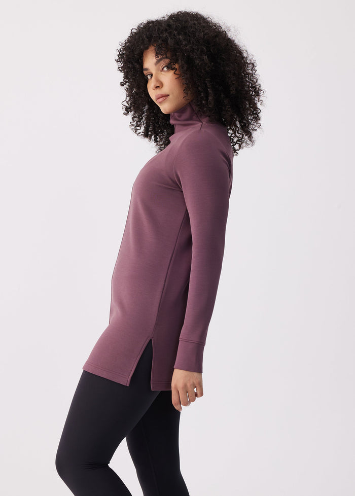 Women's long-sleeve turtleneck tunic top with side slits, paired with black leggings, side view