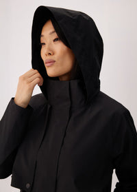 Women's black hooded trench coat close-up, model adjusting hood with hand