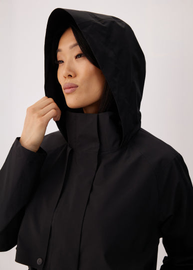 Women's black hooded trench coat close-up, model adjusting hood with hand
