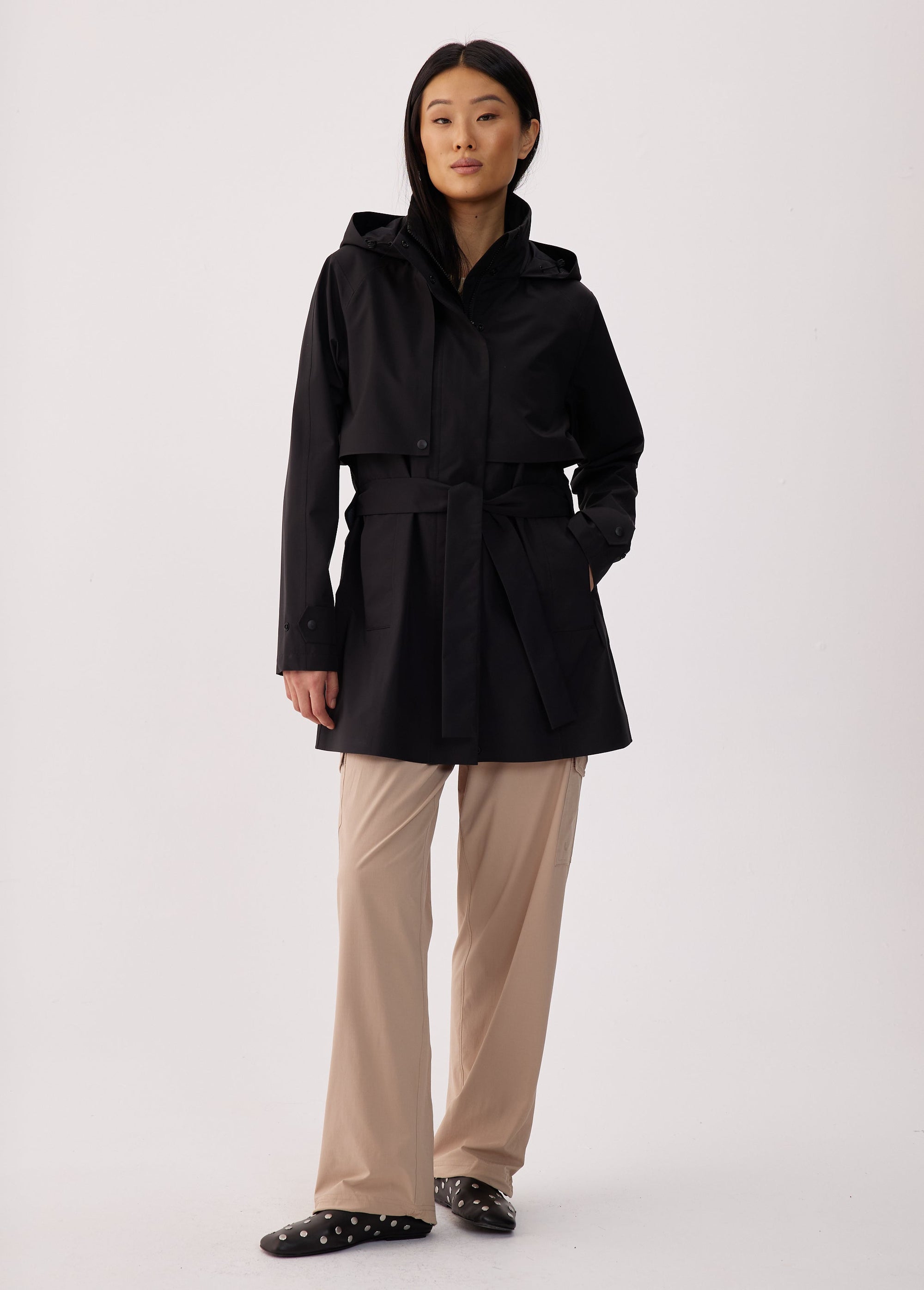 Black short trench coat with hood, belted waist, and snap buttons, front view on model