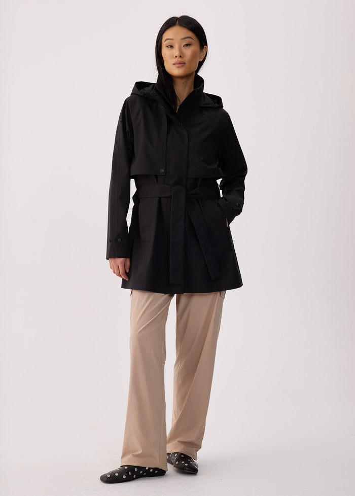 Black short trench coat with hood, belted waist, and snap buttons, front view on model
