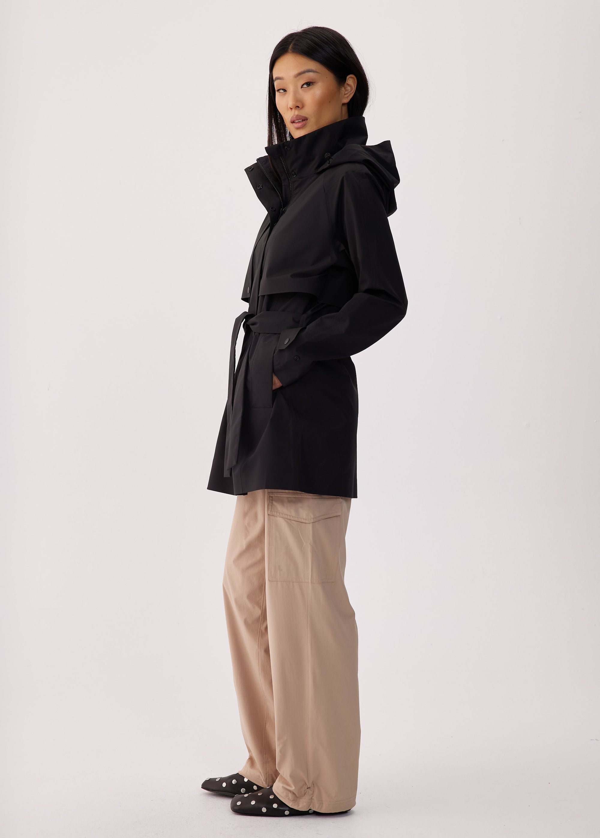Black short trench coat with hood, storm flap, and belt, side view on model