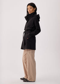 Black short trench coat with hood, storm flap, and belt, side view on model