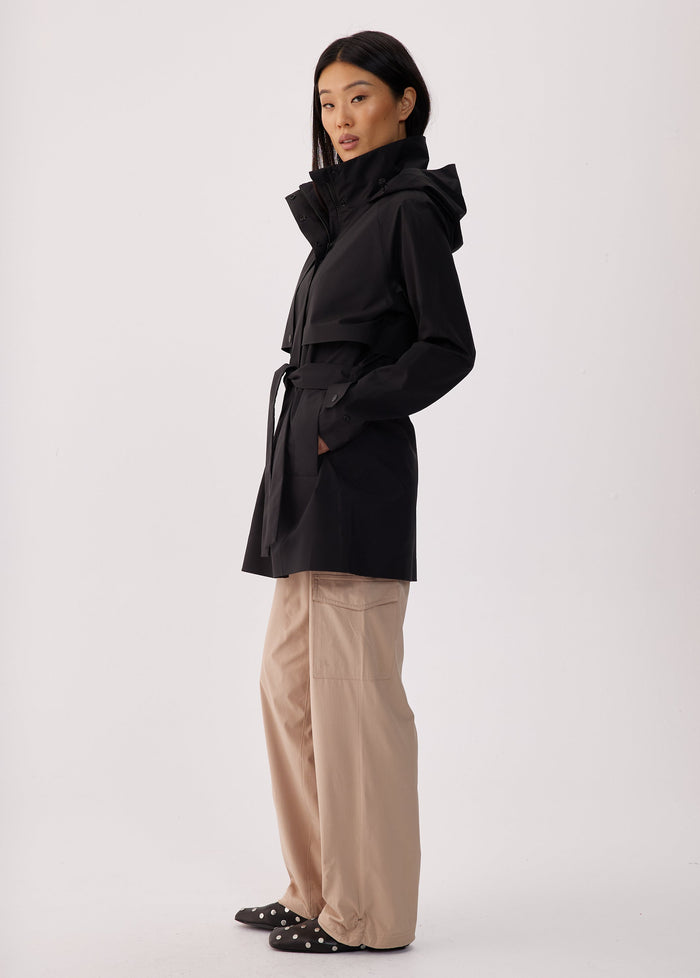 Black short trench coat with hood, storm flap, and belt, side view on model