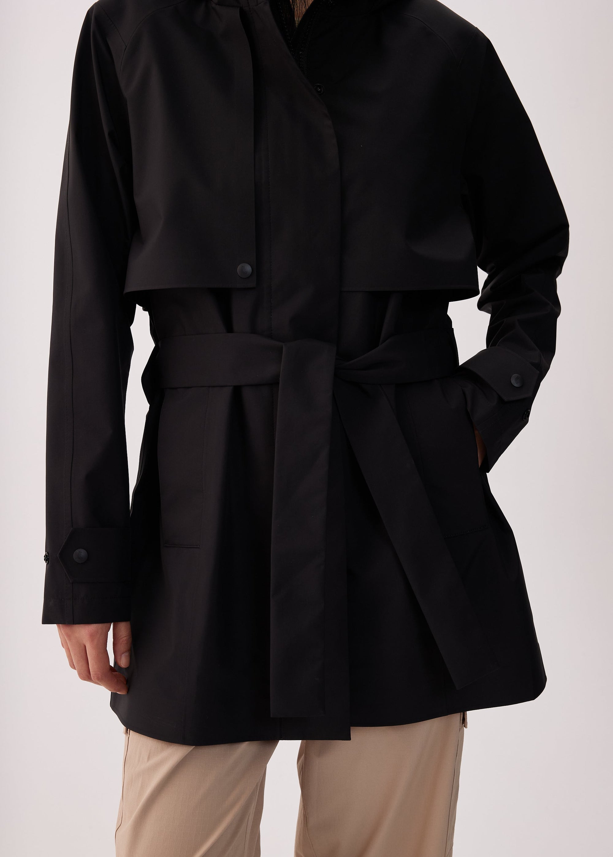 Black short trench coat with belt, snap buttons, storm flap, and button cuffs, front view