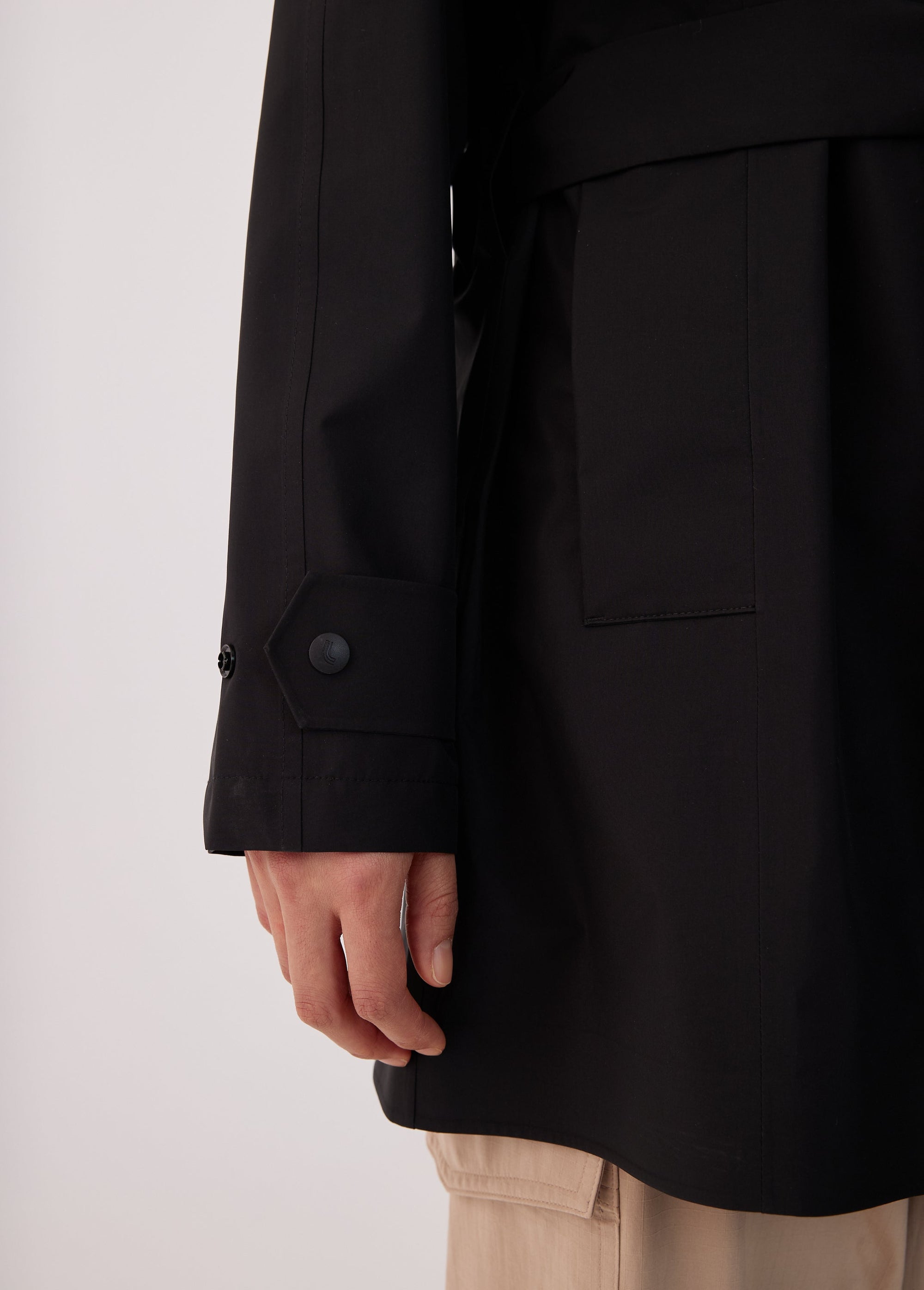 Close-up detail of black trench coat sleeve cuff with snap buttons and side patch pocket