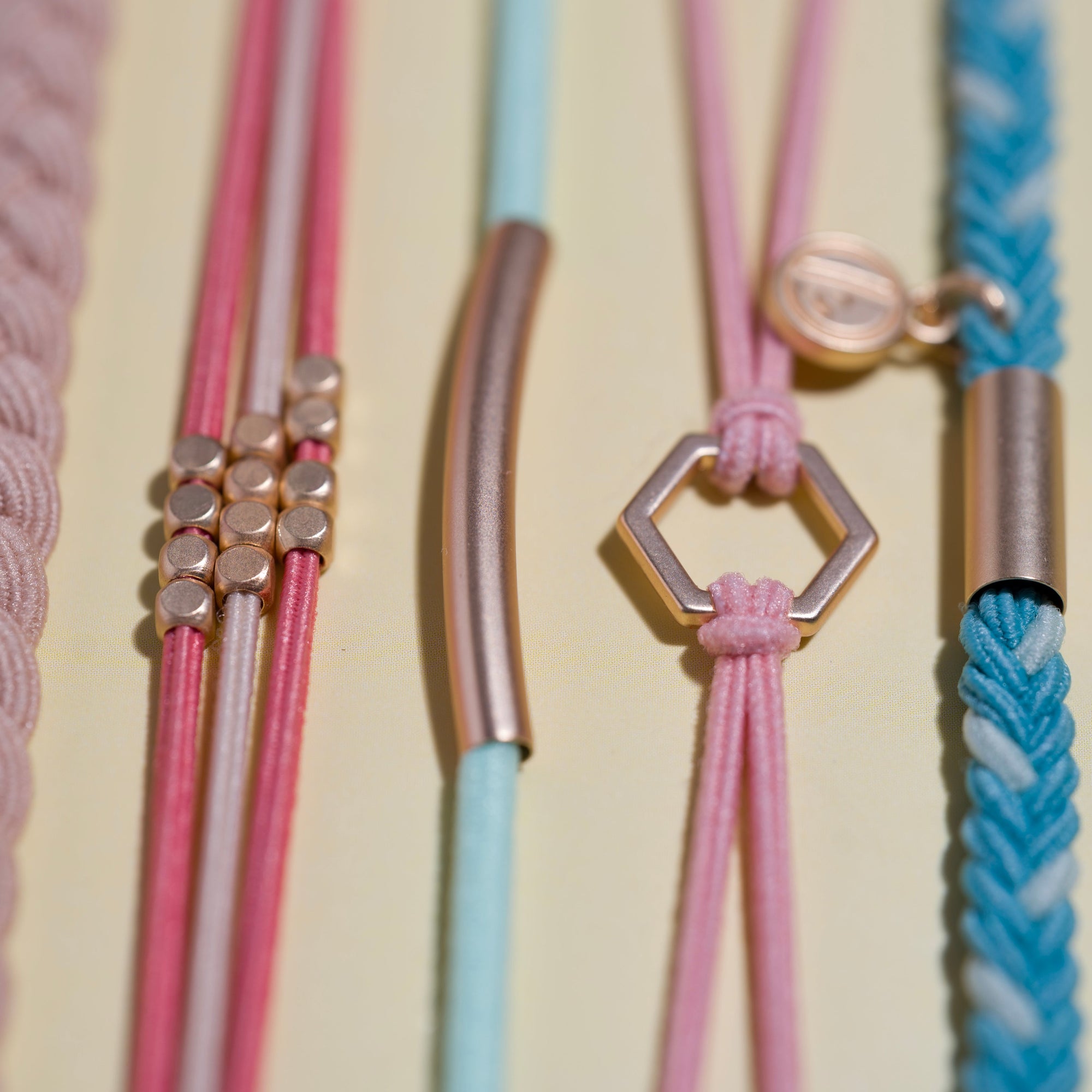 Close-up of cord bracelets with rose gold charms including hexagon pendant, tube bar, and cube beads