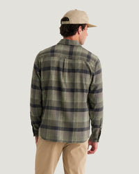 Men's plaid flannel shirt in green and navy, back view, worn with khaki pants and baseball cap