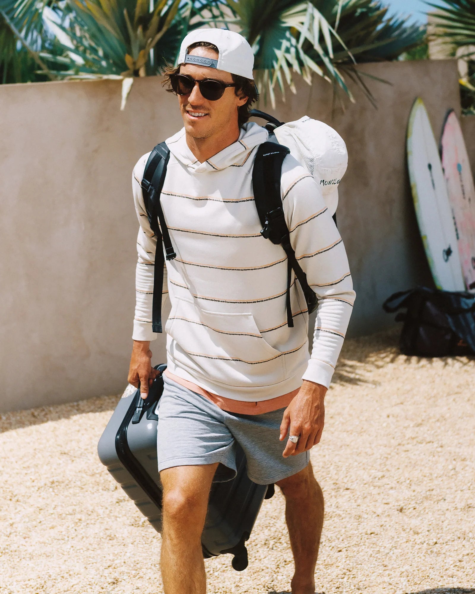Man wearing a striped lightweight pullover hoodie with backpack and luggage outdoors
