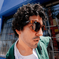 Man wearing large round tortoiseshell sunglasses with dark lenses, side profile view outdoors