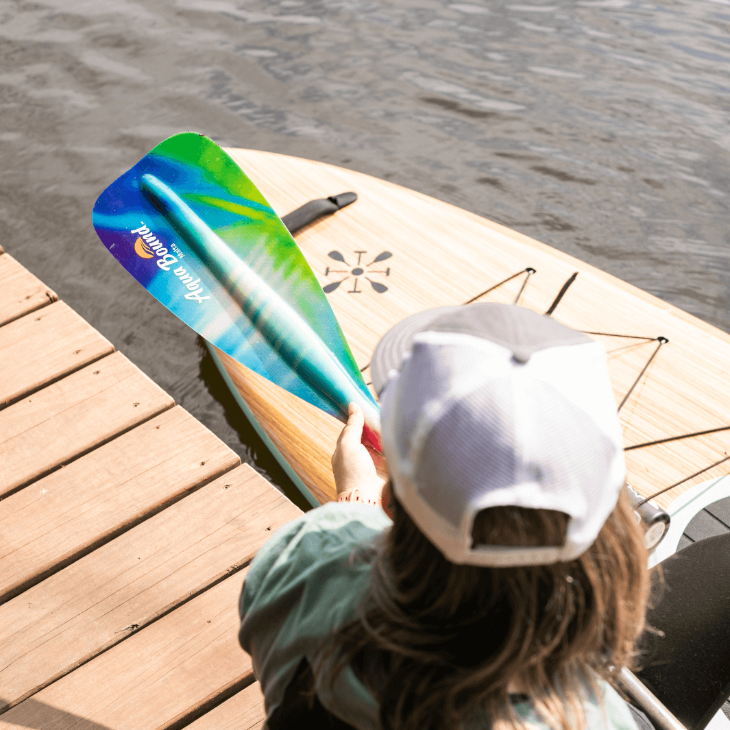 Person holding blue-green gradient fiberglass paddle blade on wooden dock over water