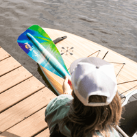 Person holding blue-green gradient fiberglass paddle blade on wooden dock over water
