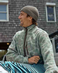 Man wearing camo fleece half-zip pullover, smiling outdoors, three-quarter view
