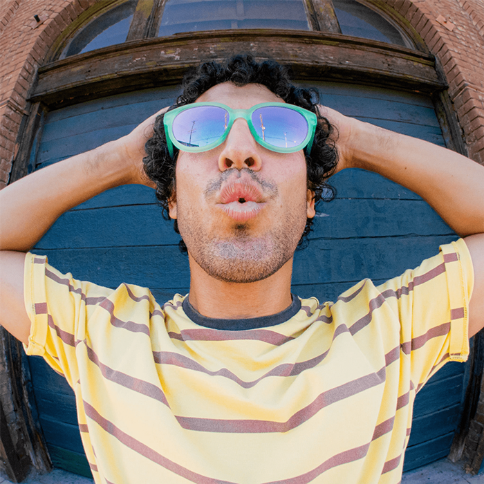 Person wearing oversized wayfarer-style sunglasses with mint green frames and blue mirrored lenses