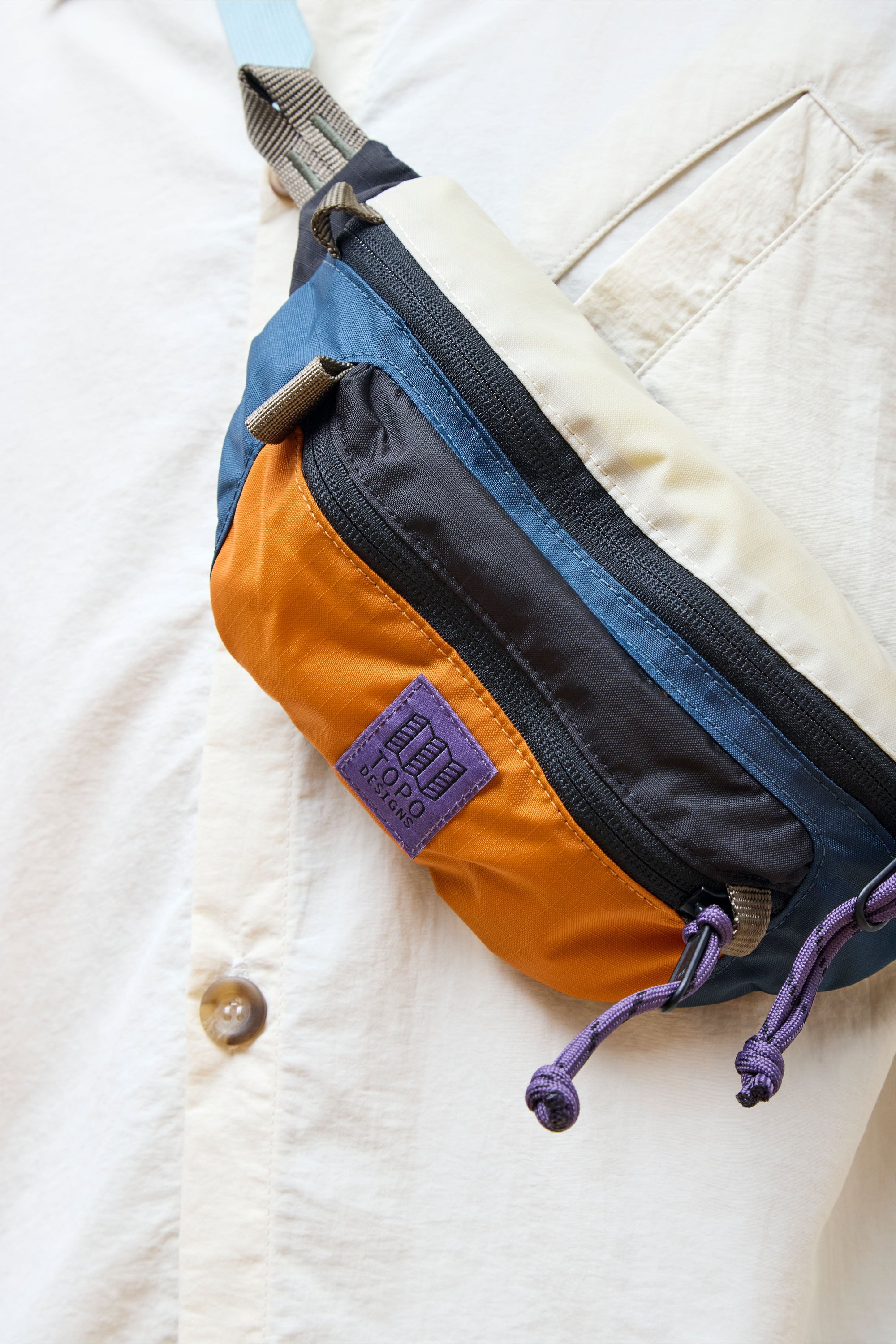 Colorblock waist pack with blue and orange panels, purple drawcords and brand label