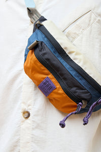 Colorblock waist pack with blue and orange panels, purple drawcords and brand label