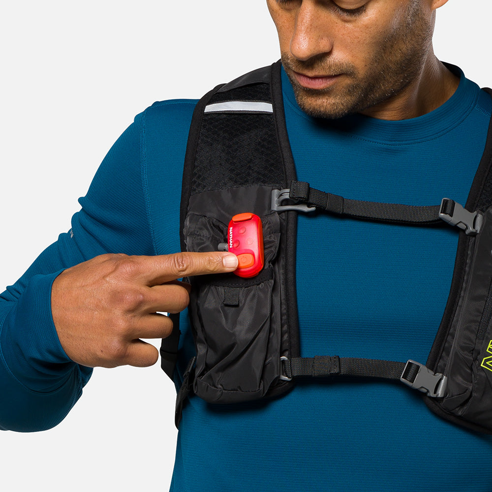 Red LED safety light clipped to black chest harness worn by person in blue shirt