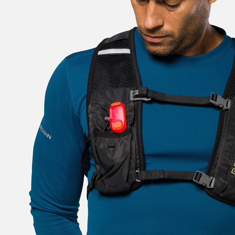 Red LED safety light clipped to black running vest strap on runner's chest