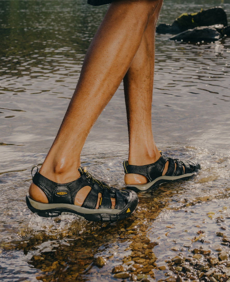 Water sandals with protective toe coverage worn while walking through shallow water over rocky streambed