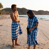 Two people on beach wearing blue and white wavy striped towels at sunset