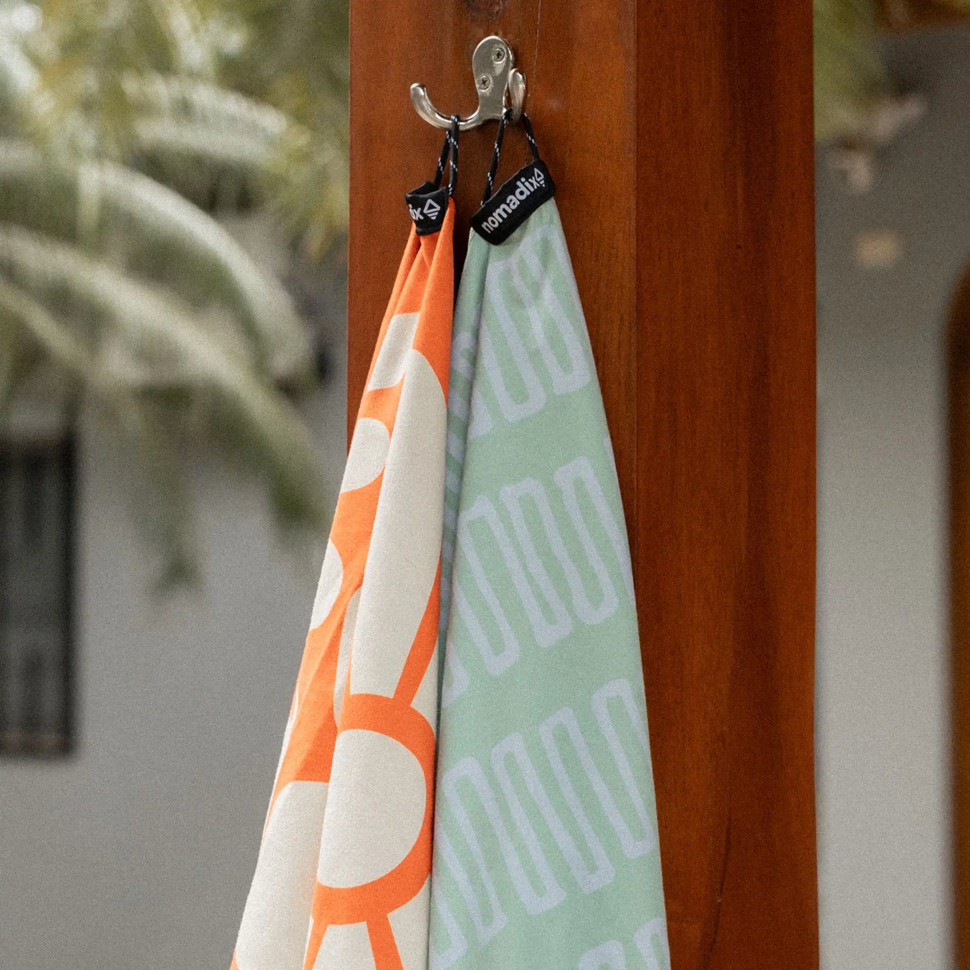 Two microfiber towels hanging on wooden post, one orange and white, one seafoam green with text