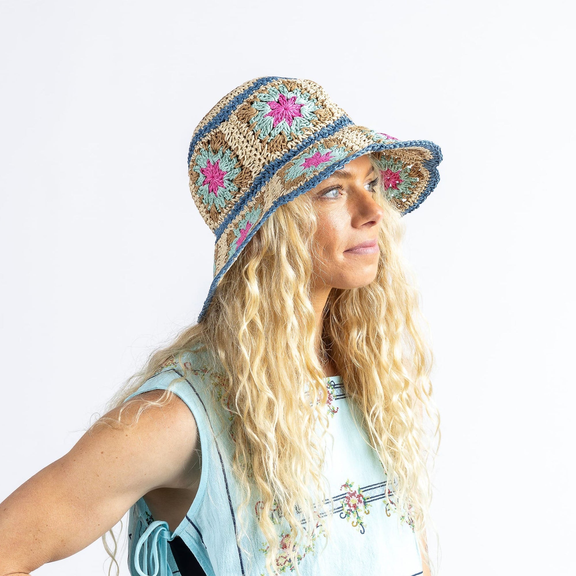 Crochet bucket hat with floral granny squares in tan, blue, and pink, worn by model