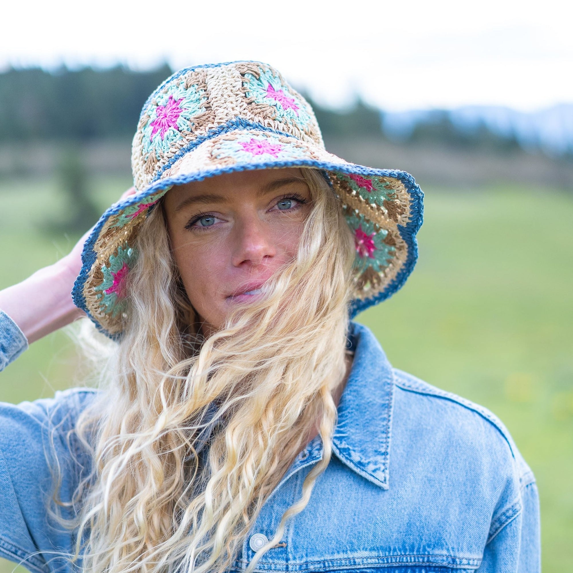 Crochet straw bucket hat with blue trim and colorful floral pattern, worn on model outdoors