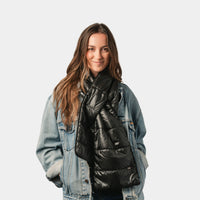 Black quilted puffer scarf worn draped around neck over denim jacket, on-model front view