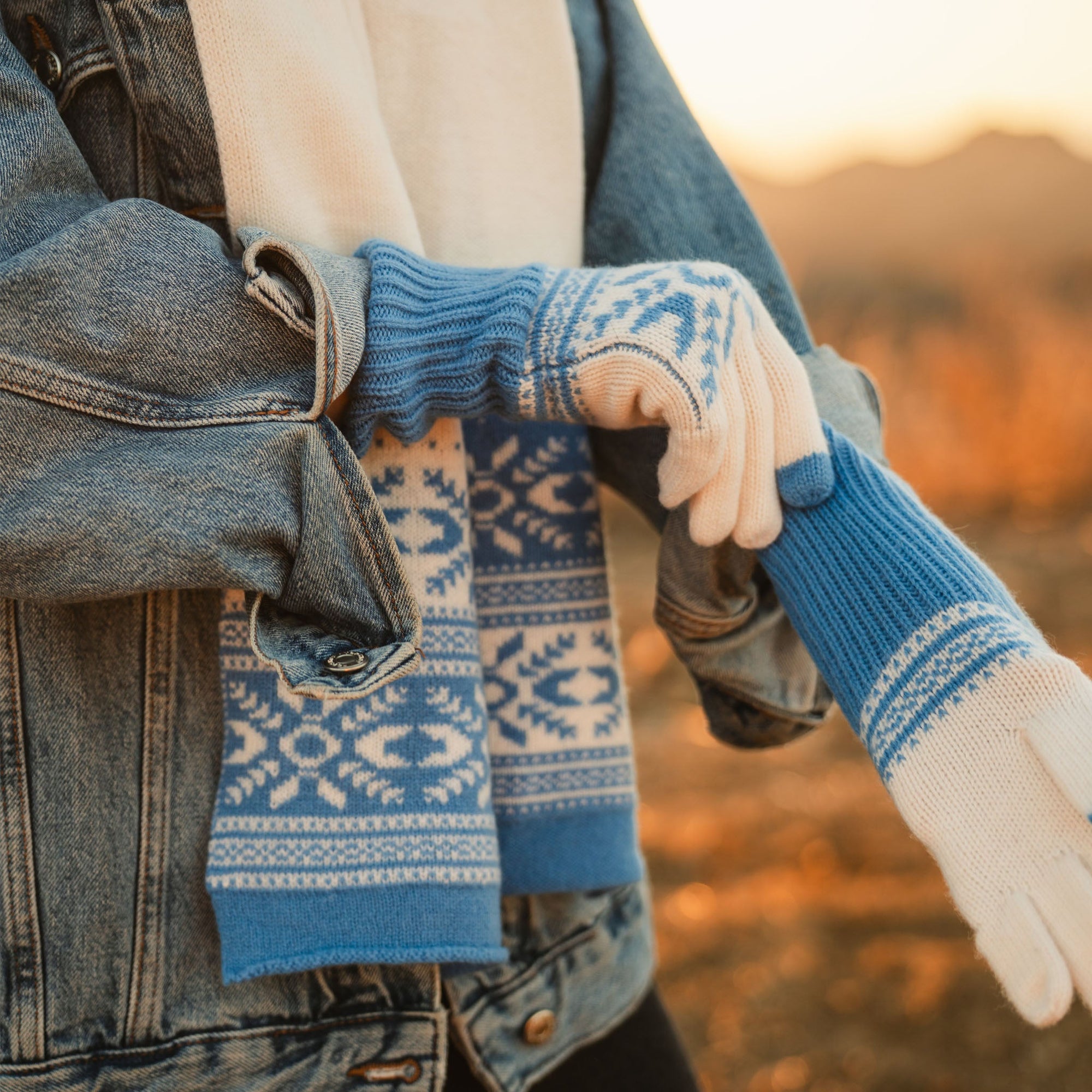 Blue and cream Fair Isle knit gloves with Nordic pattern, worn outdoors at sunset