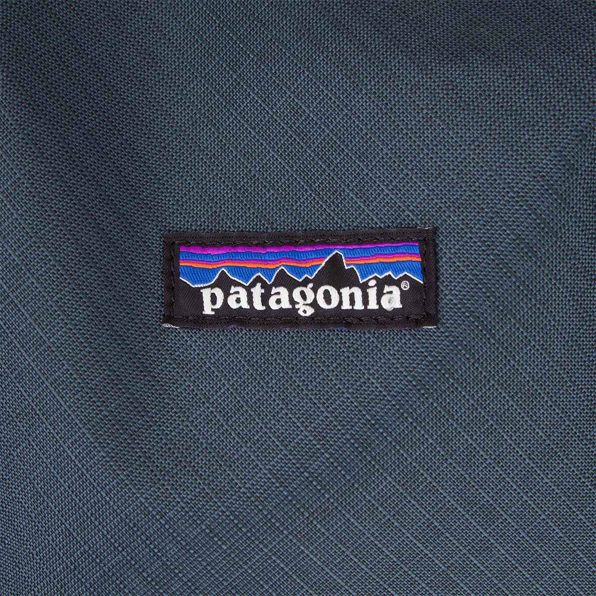 Close-up detail shot of a woven brand logo patch on a blue-grey cube bag