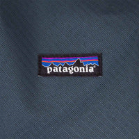 Close-up detail shot of a woven brand logo patch on a blue-grey cube bag