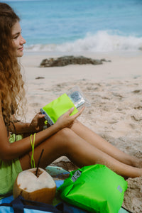 Woman on beach holding bright green waterproof phone case with clear viewing window