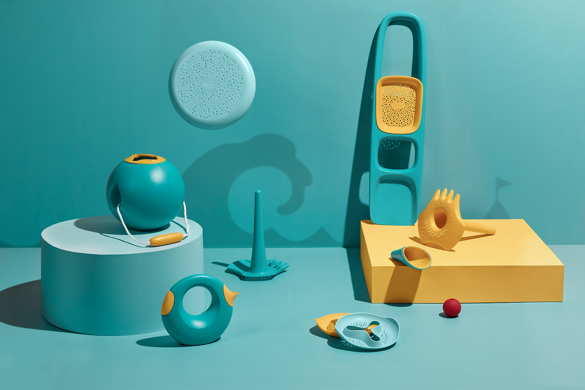 Beach toy set with bucket, scoops, and strainers in teal and yellow colors on studio background