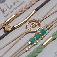 Close-up of multiple hair tie bracelets with gold charms, wave pendant, teal beads, and braided cords