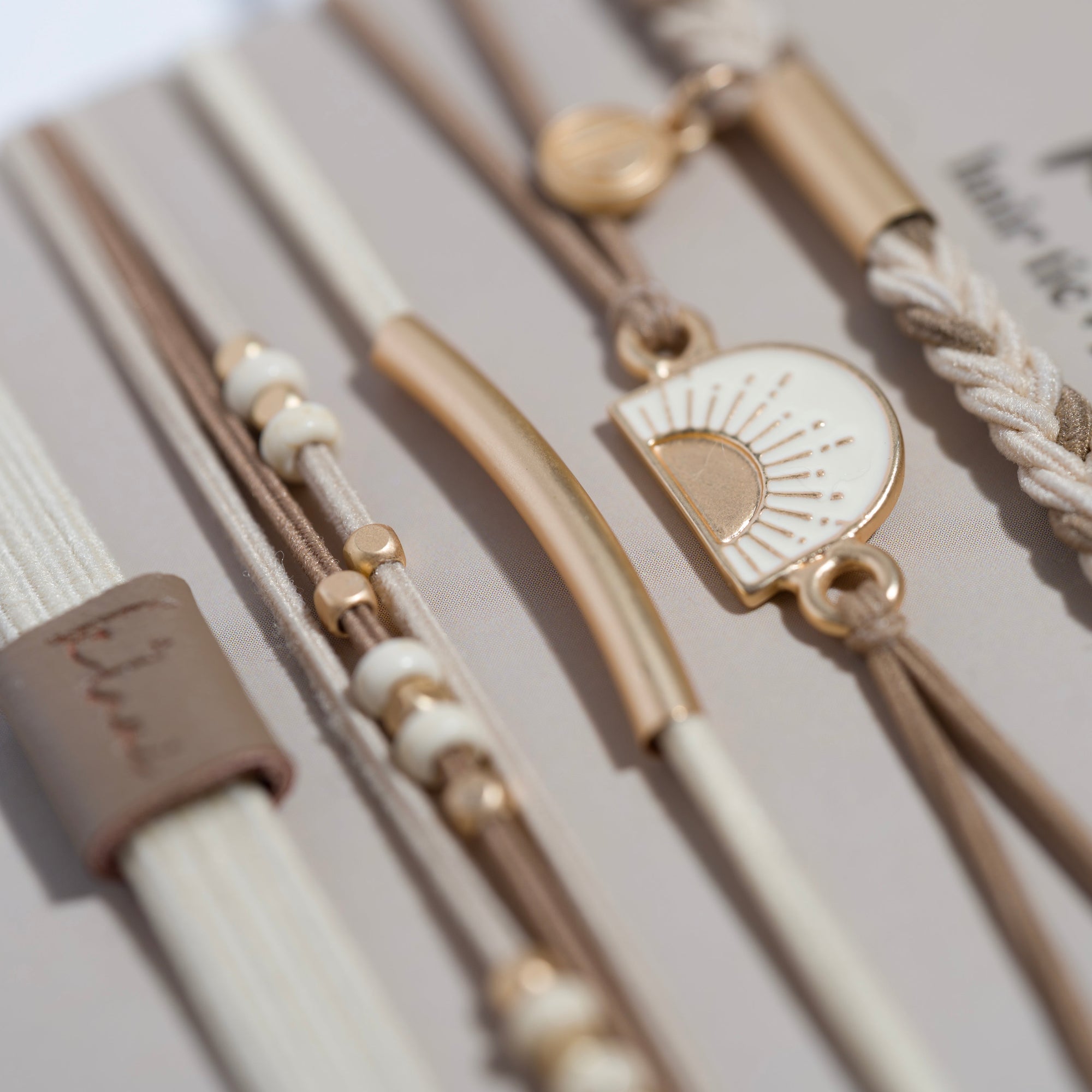 Set of hair tie bracelets with gold charms including a sun motif, beads, and braided cord