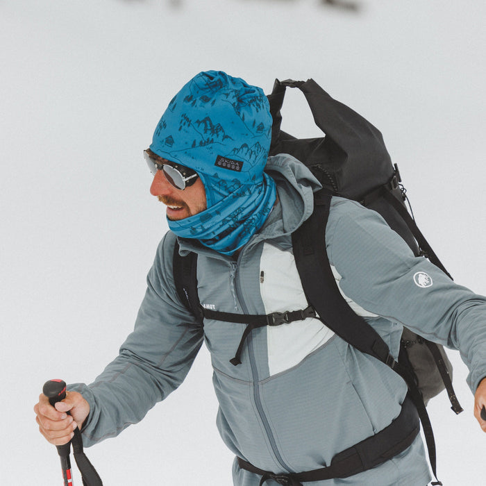 Men's alpine hat with mountain print pattern worn on model with neck gaiter, side view