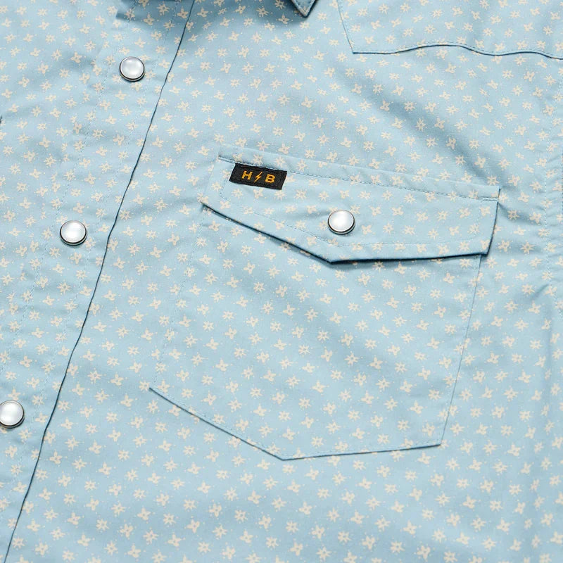 Close-up detail of light blue floral snap shirt showing chest pocket and pearl snap buttons
