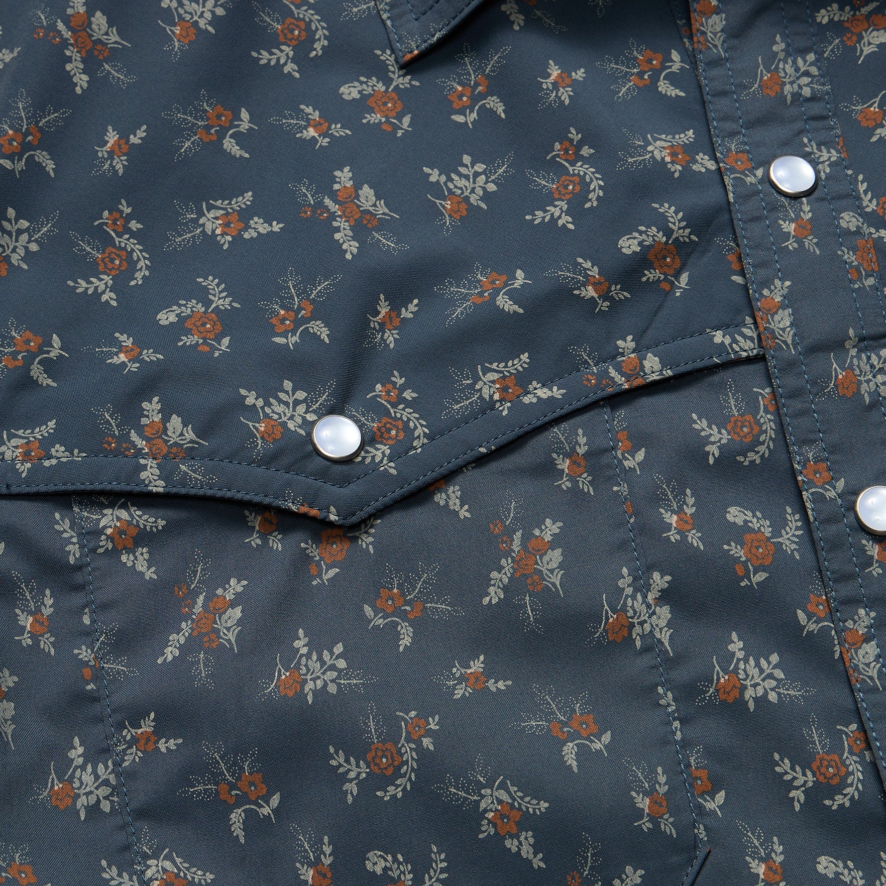 Close-up of dark blue shirt with small floral print showing snap buttons and chest pocket details