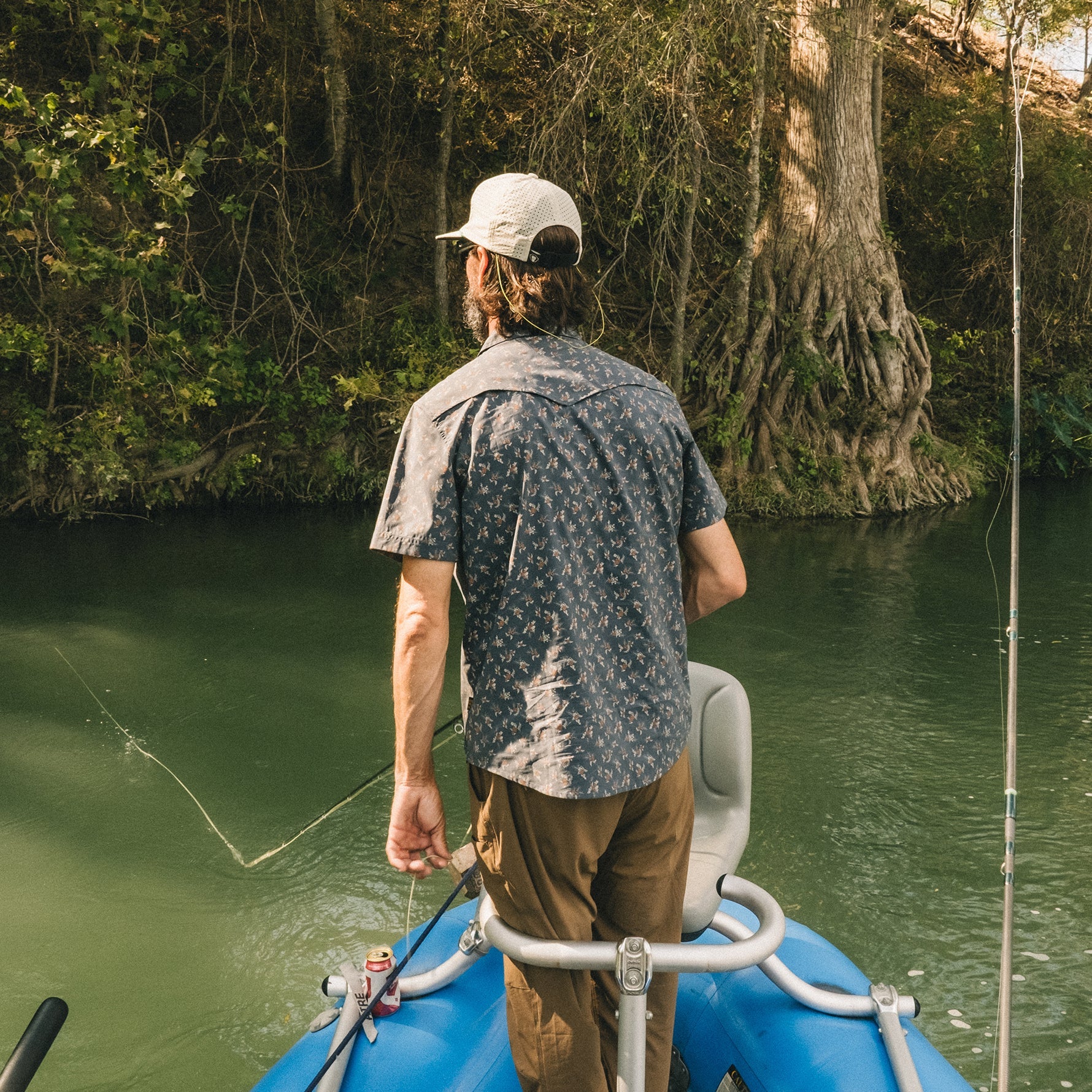 Man in patterned short-sleeve shirt fishing from boat on green water