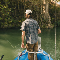 Man in patterned short-sleeve shirt fishing from boat on green water